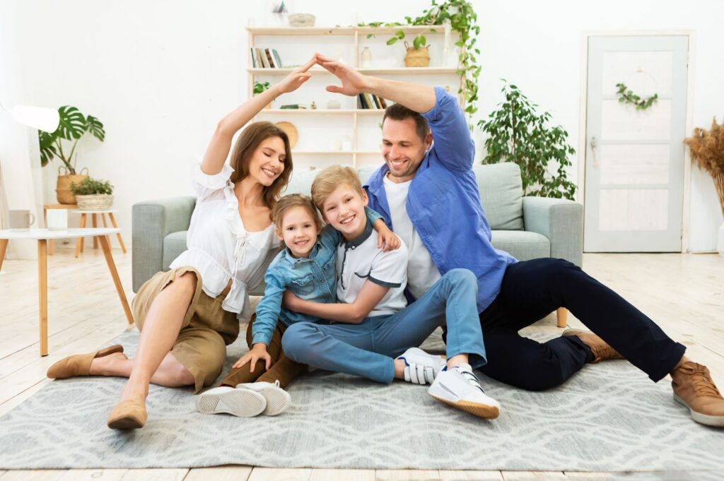 A happy family of four sits on the floor, forming a heart shape with their arms.