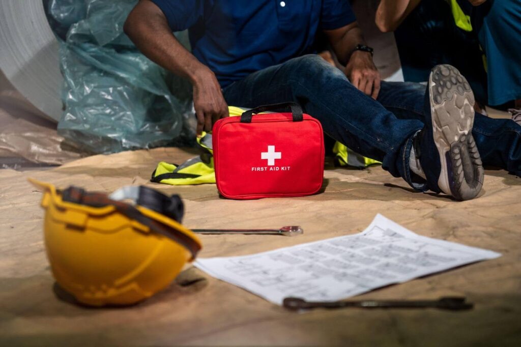 A man sitting on the ground with a first aid kit beside him ready to assist with medical needs