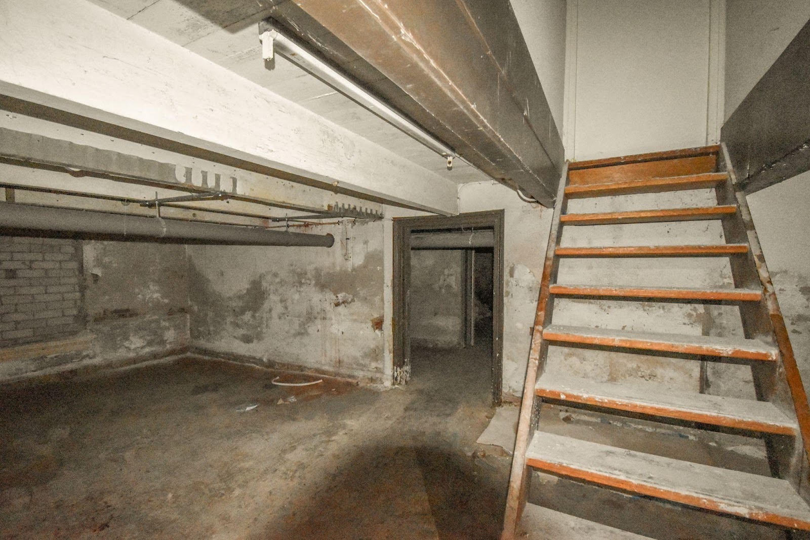 An empty room featuring a ladder against the wall and a staircase leading to an upper level