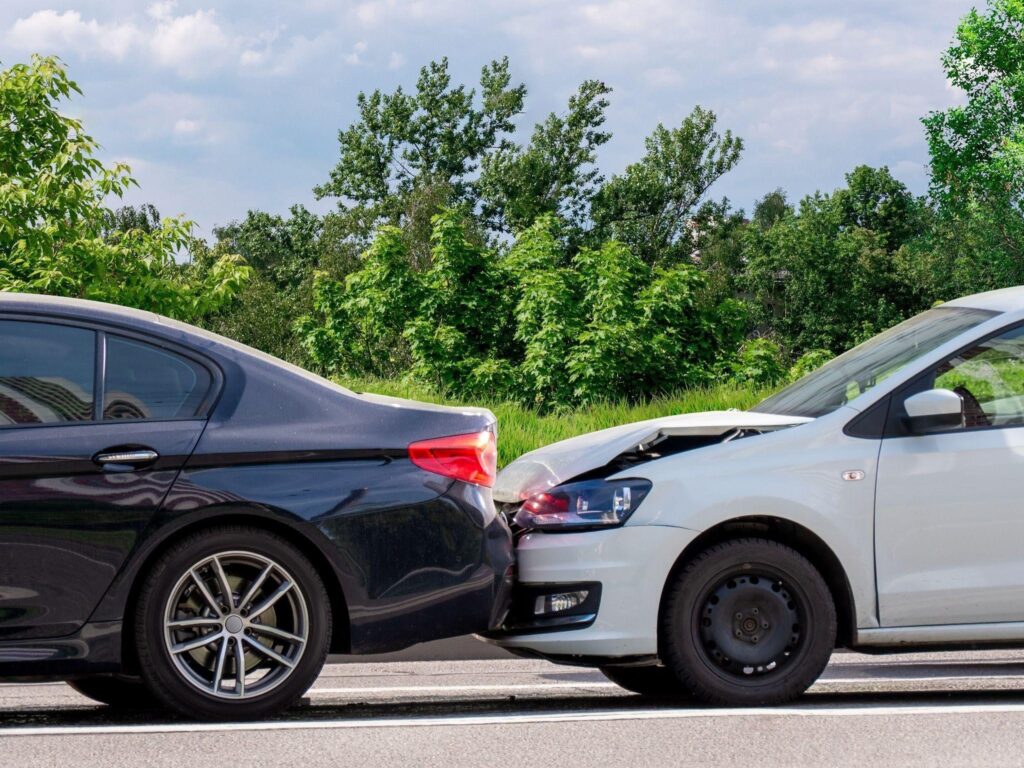 Two damaged cars after a collision with visible dents and broken parts parked on the roadside