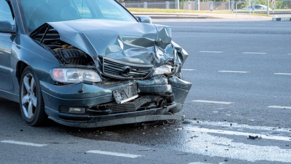 A car with significant body damage and a broken headlight showing the aftermath of a collision