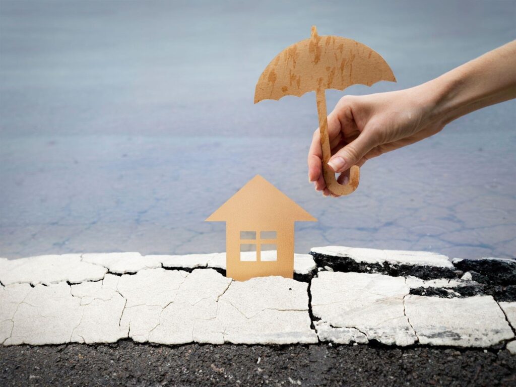 A person holding an umbrella over a paper house in the rain
