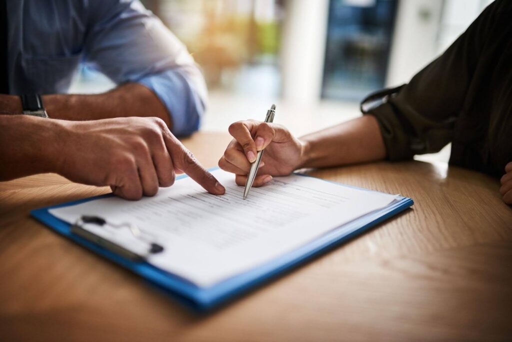 A couple signing a contract at a table focused on the document with pens in hand