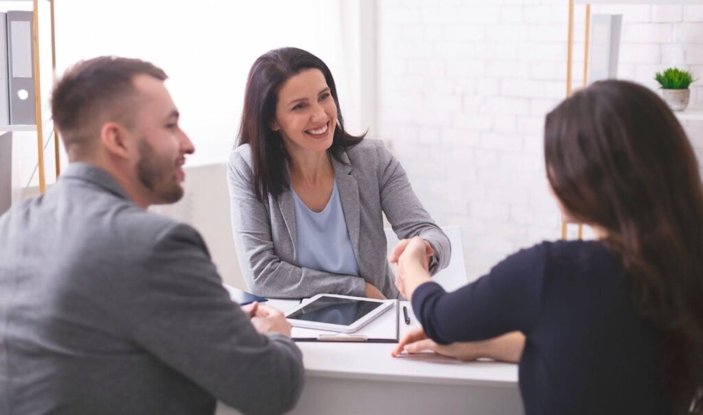 A man and woman shaking hands over a desk symbolizing a professional agreement or collaboration